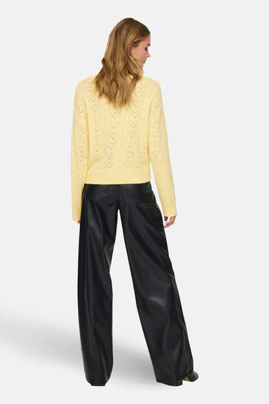 Gele rondehals-trui van ONLY, met hartvormig ajourpatroon, gedragen met een zwarte wijde broek.