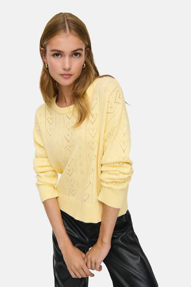 Gele rondehals-trui van ONLY, met ajourpatroon en gedragen met een zwarte broek.