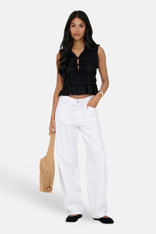 Jean droit blanc de ONLY, porté avec un top noir noué et des ballerines, avec un sac en filet.
