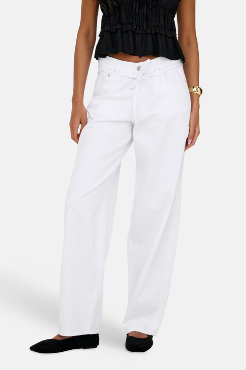 Jean droit en denim blanc de ONLY, porté avec un haut noir à volants et un bracelet doré.