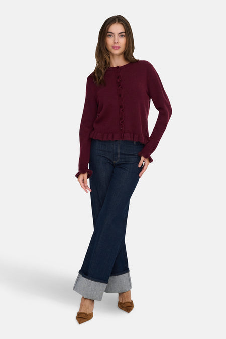 Cardigan bordeaux en maille fine de JDY, avec boutons et détails à volants, porté avec un jean taille haute.
