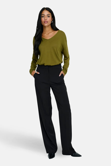 Pull à col en V vert de JDY, porté avec un pantalon noir ample.
