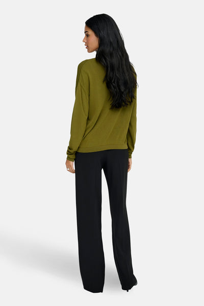 Pull à col en V vert de JDY, porté avec un pantalon noir fluide, vue de dos.
