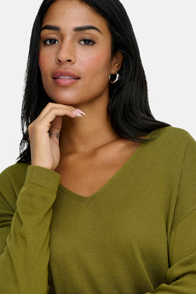 Groene V-hals trui van JDY, gedragen door een vrouw met zilveren oorbellen.