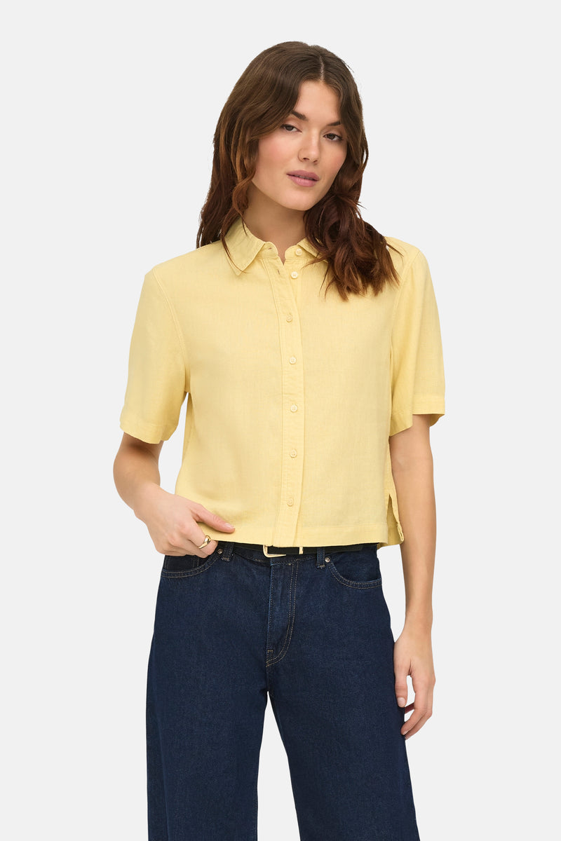 Chemise jaune à manches courtes par ONLY, portée avec un jean taille haute et une ceinture noire.
