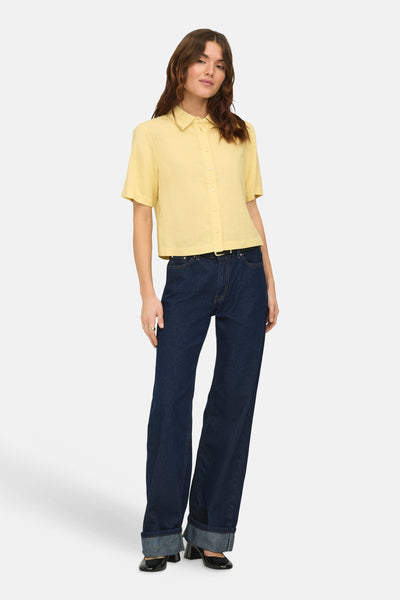 Chemise jaune à manches courtes de ONLY, portée avec un jean bleu foncé et des chaussures noires à talons.