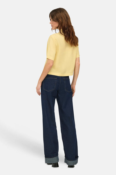 Chemise jaune à manches courtes de ONLY, portée avec un jean ample bleu marine et des chaussures noires à talons.
