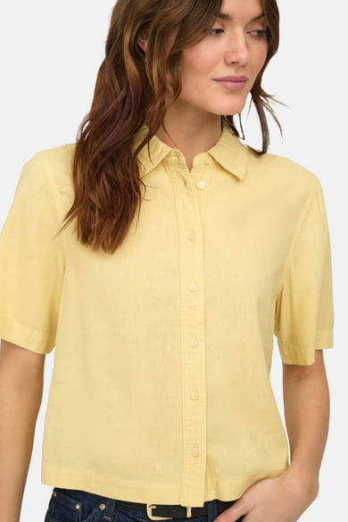 Chemisier jaune à manches courtes de ONLY, porté avec un jean à ceinture noire.
