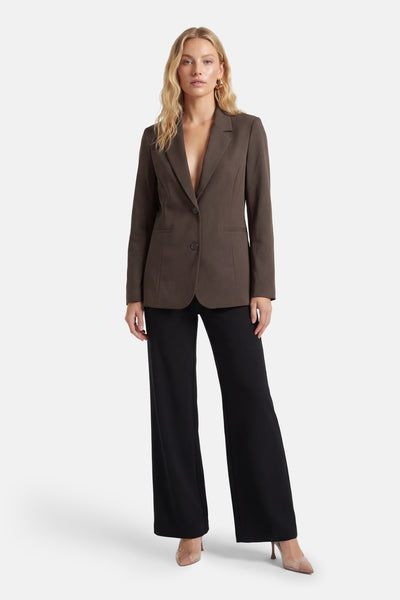 Blazer brun ONLY® avec une fermeture boutonnée, porté avec un pantalon noir taille haute et des escarpins nude.
