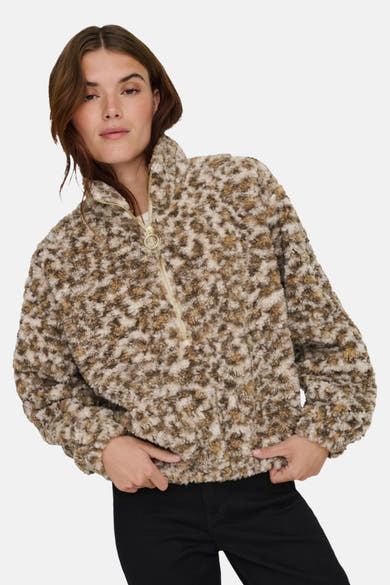 Korte beige jas van pluizige stof van ONLY, met gouden ritssluiting aan de voorkant en gedragen over een zwarte broek.