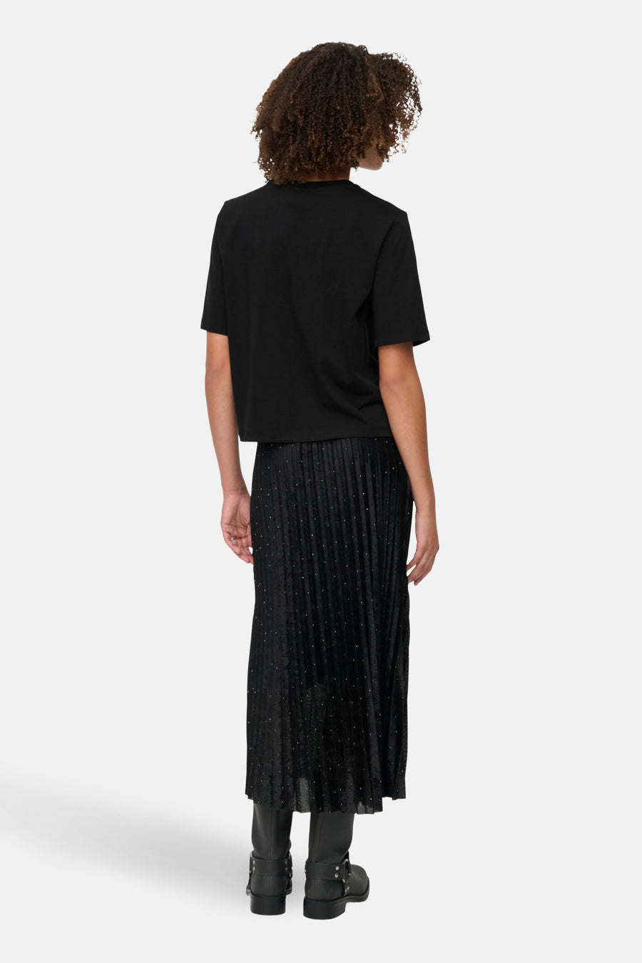 Zwart T-shirt met korte mouwen van ONLY, gedragen met een lange, geplooide zwarte stippenrok en laarzen.