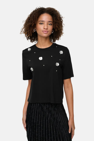 Zwart T-shirt met korte mouwen van ONLY, versierd met zilveren bloemen en strass, gedragen met een geplooide rok.