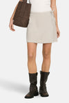 Korte beige rok van ONLY®, wikkelmodel, gedragen met een wit T-shirt met hart en donkerbruine bikerlaarzen.