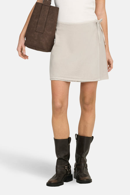 Jupe courte beige de ONLY, avec une ceinture à nouer sur le côté, portée avec des bottes en cuir marron et un sac à main.
