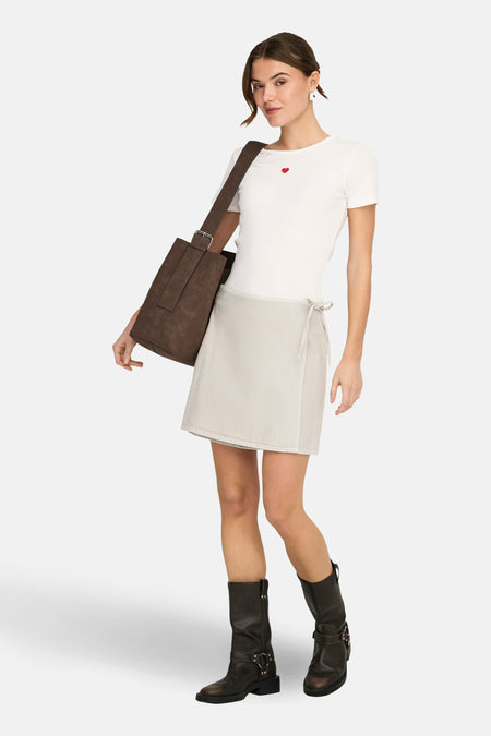 Jupe courte beige de ONLY®, style portefeuille, portée avec un t-shirt blanc à cœur et des bottes motard marron foncé.