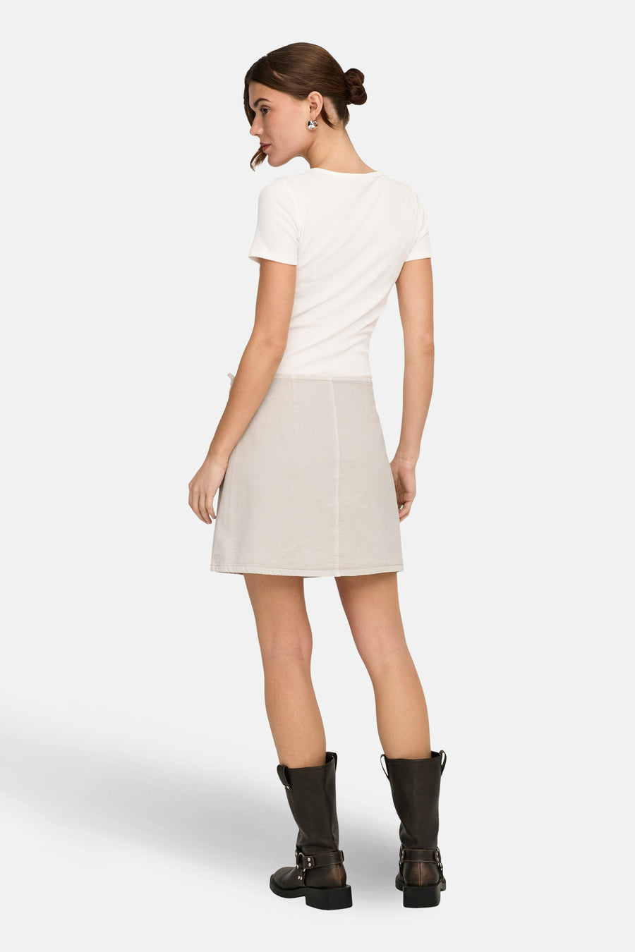 Korte beige rok van ONLY, met een subtiele textuur, gecombineerd met een wit T-shirt en bruine leren laarzen, van achteren gezien.