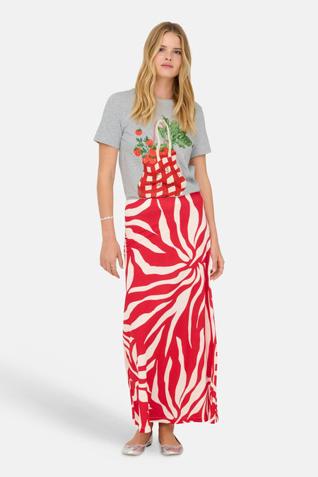 T-shirt gris à manches courtes de ONLY, imprimé d'un sac rempli de légumes, porté avec une longue jupe à motif zébré rouge et blanc.
