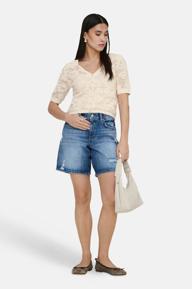 Gilet écru de ONLY®, avec un motif ajouré, porté avec un short en jean délavé et des ballerines.
