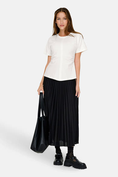 Top uni manches courtes blanc de ONLY, porté avec une jupe plissée noire, des chaussettes à dentelle et des chaussures épaisses.