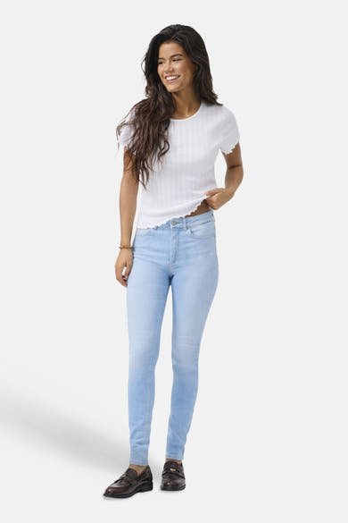 Skinny jeans in lichtblauw denim van ONLY, gedragen met een wit T-shirt en bruine loafers.