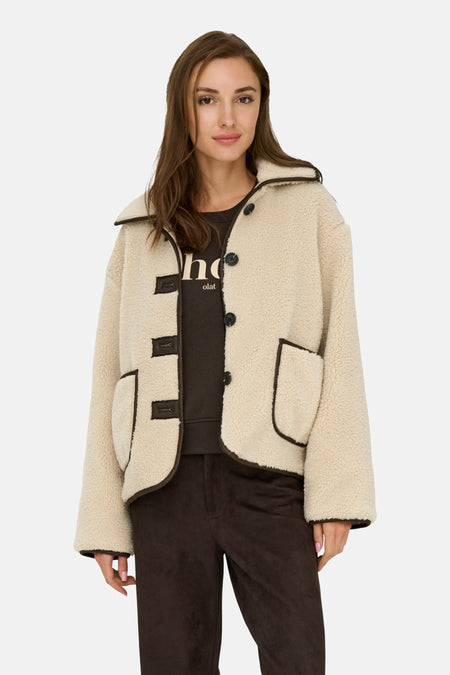 Veste courte écru de JDY avec bordure contrastante et fermeture boutonnée, portée avec un pantalon marron.