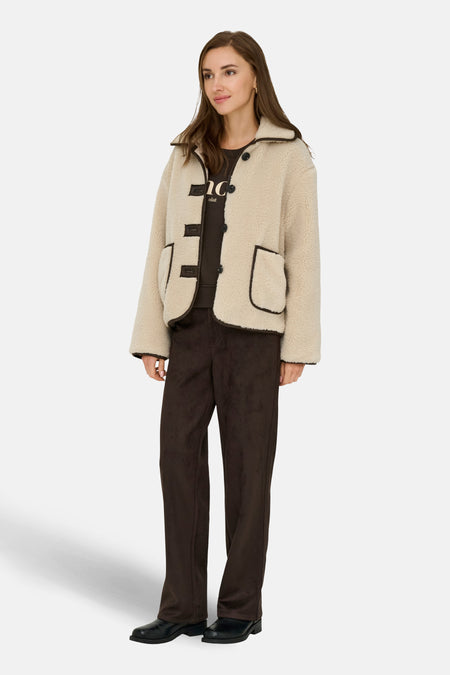 Veste courte écru de JDY avec finitions marron foncé, portée avec un pantalon marron et des chaussures noires.