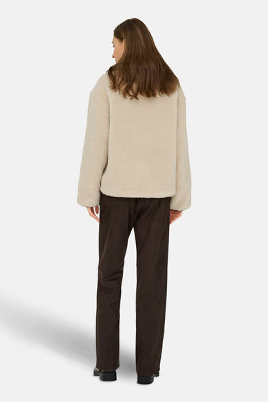 Veste courte écru de JDY, avec une texture bouclée, portée avec un pantalon marron.