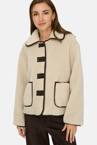 Veste courte écru de JDY, avec bordure marron et boutons apparents, portée avec un pantalon marron.
