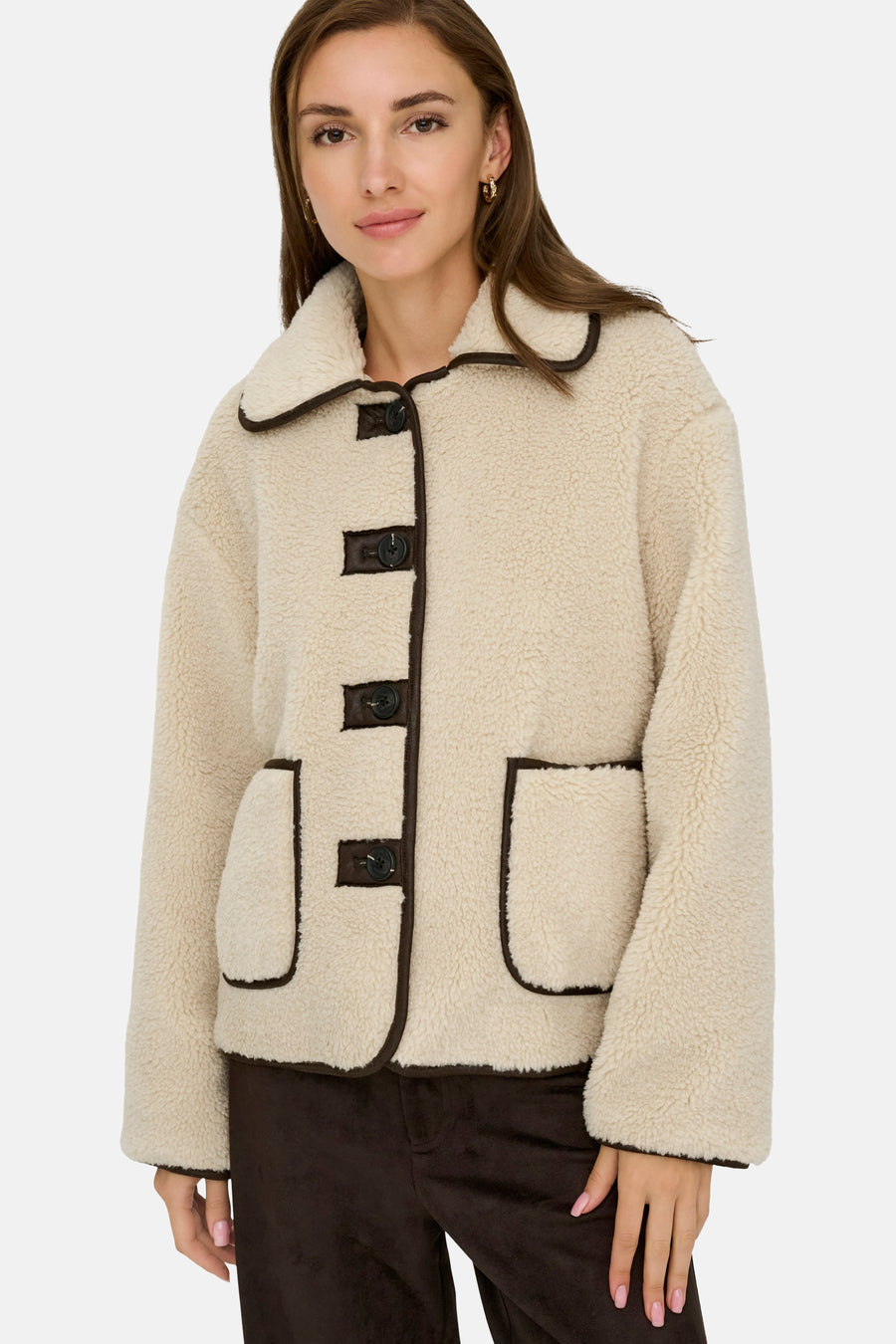 Veste courte écru de JDY, avec bordure marron et boutons apparents, portée avec un pantalon marron.
