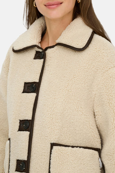 Veste courte écru par JDY, détails en similicuir marron, fermeture boutonnée et texture bouclée visible.