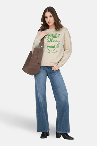 Sweat-shirt écru de ONLY®, avec motif imprimé Matcha, porté avec un jean large et des bottines noires.
