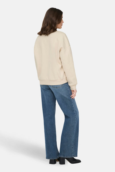 Ecru sweatshirt van ONLY®, gedragen met een wijde blauwe jeans en zwarte enkellaarsjes met hak.