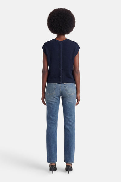 T-shirt bleu de JDY, vue de dos, à la texture tricotée avec des boutons le long du dos, porté avec un jean et des mules noires.