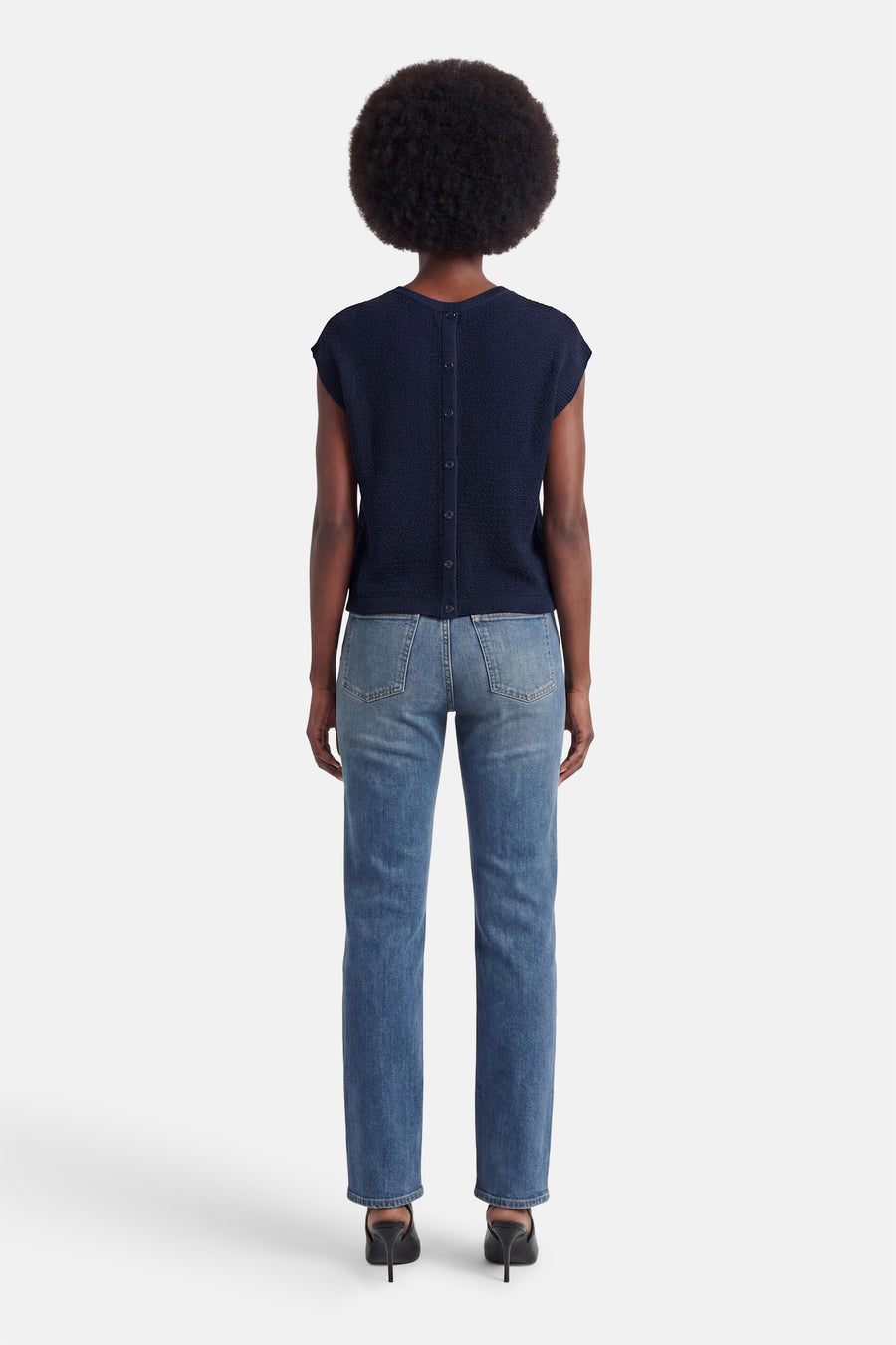 T-shirt bleu de JDY, vue de dos, à la texture tricotée avec des boutons le long du dos, porté avec un jean et des mules noires.