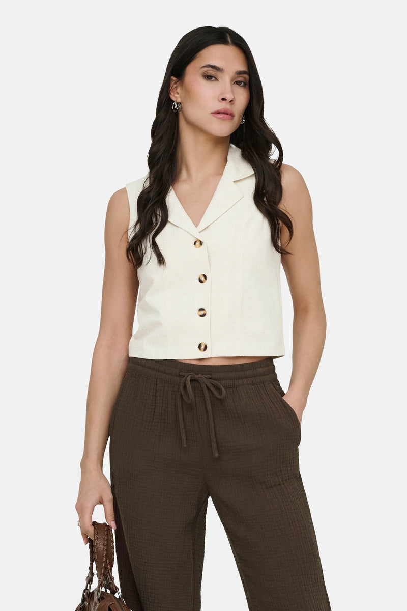 Beige blazer van JDY, mouwloos, met knoopsluiting aan de voorkant, gedragen met een bruine broek en een leren handtas.