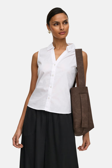 Chemisier blanc sans manches de JDY, col à revers et boutonnage frontal, porté avec une jupe noire et un sac marron.