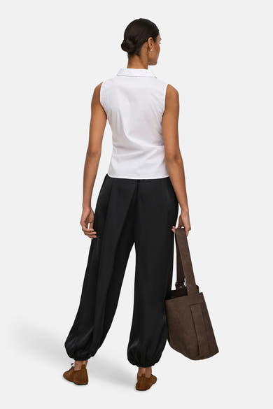 Chemisier blanc sans manches de JDY, porté de dos avec un pantalon noir ample, des chaussures marron et un sac cabas.