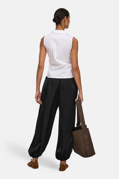 Chemisier blanc sans manches de JDY, porté de dos avec un pantalon noir ample, des chaussures marron et un sac cabas.