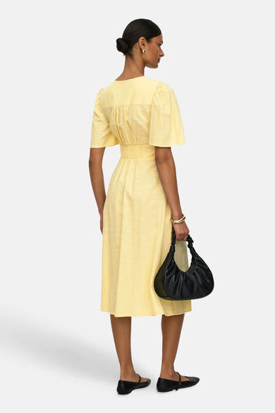 Robe jaune de JDY avec manches courtes, détail froncé et sac à main noir.
