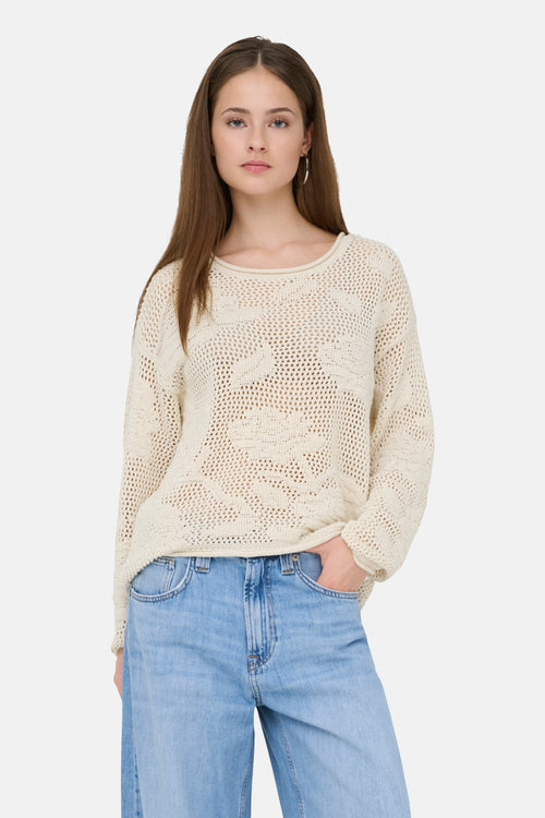 Pull à col rond écru de ONLY, en maille ajourée, porté avec un jean taille haute.
