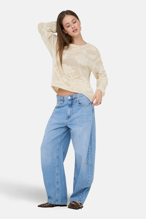 Pull à col rond écru de ONLY®, en maille ajourée, porté avec un jean ample et des mules imprimées léopard.
