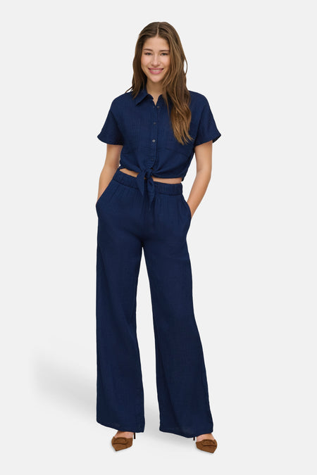 Chemise bleue à manches courtes de ONLY, nouée à la taille, portée avec un pantalon bleu assorti et des escarpins marron.