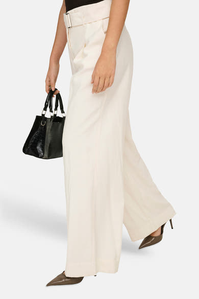 Pantalon large fluide beige de ONLY® avec ceinture à boucle, poches et plis, porté avec un sac noir et des escarpins marron.