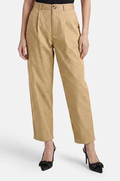 Pantalon beige de ONLY®, plissé sur le devant avec fermeture boutonnée et ourlets retroussés, porté avec des escarpins noirs à nœud.