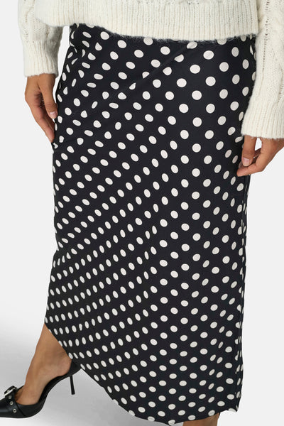 Jupe noire mi-longue de ONLY, à motif à pois blancs, portée avec un pull en maille écrue.