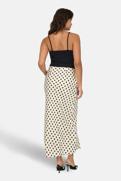Jupe midi écru à pois noirs de ONLY, portée avec un débardeur noir et des mules à talons hauts.
