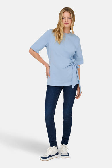 T-shirt bleu à manches courtes de ONLY, noué sur le côté, porté avec un jean foncé et des baskets blanches.
