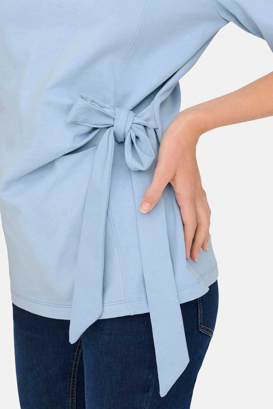 T-shirt bleu à manches courtes de ONLY®, avec un nœud décoratif sur le côté et porté avec un jean bleu foncé.
