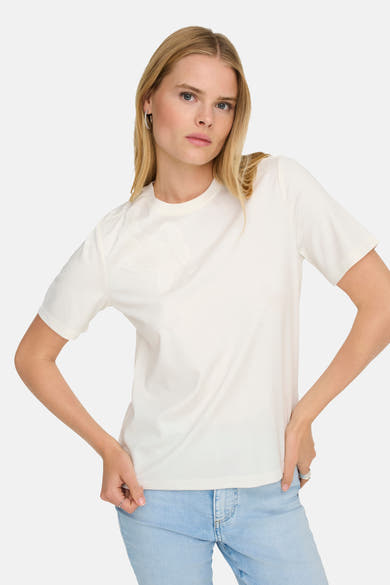 T-shirt blanc à manches courtes de ONLY, avec une fleur brodée et porté avec un jean bleu clair.
