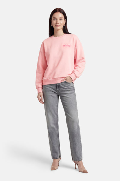 Sweat-shirt rose de ONLY®, avec un message décoratif, porté avec un jean gris et des talons hauts.